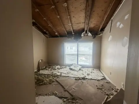A bedroom with the ceiling drywall collapsed onto the floor, exposing joists and insulation