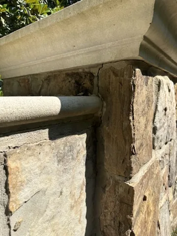 Close-up of a stone entrance column with an open joint beneath its cast stone cap