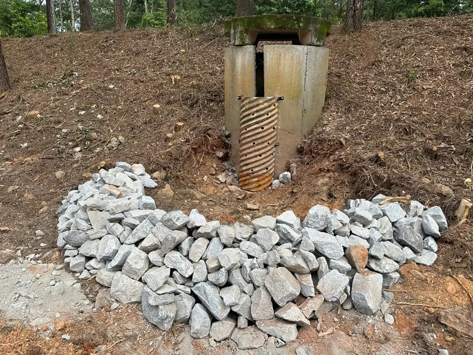 The repaired stormwater outlet with a new corrugated pipe section and a bed of riprap stone below it
